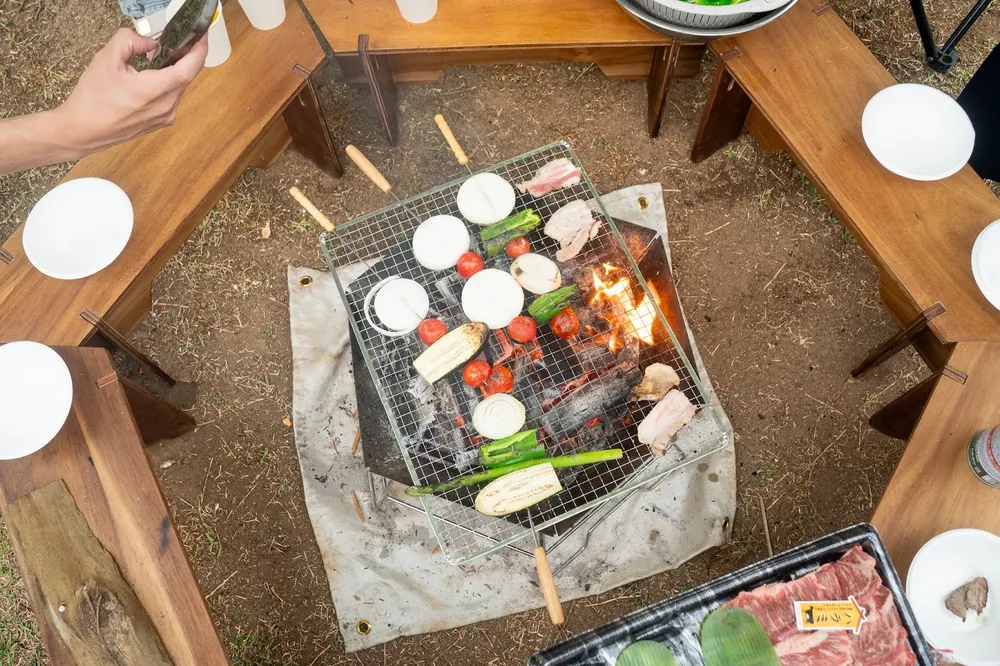 テーブルに置いた焚き火台と網で調理するようす