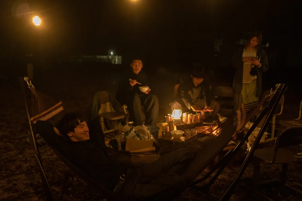 夜の校庭で、ランタンの灯りとたき火を囲んでくつろぐ人たち