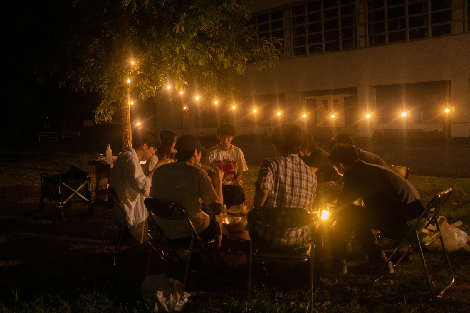 夜の校庭で開かれる芋煮会。電球のあかりの下に人が集う